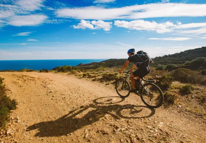 Ciclista disfruta de rutas en bici con encanto por la costa mediterránea. El mar azul y el cielo despejado acompañan su aventura.