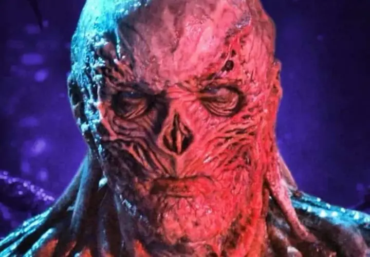 Le visage déformé et rougeaud de Vecna, le monstre de Stranger Things, se détache sur un fond violet.