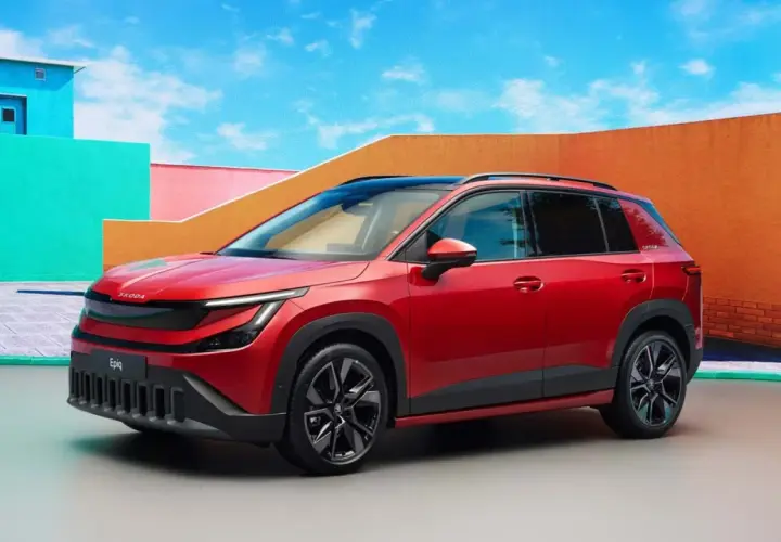 La Skoda Epiq rossa, un SUV compatto, si presenta con un design audace e moderno, circondata da un'architettura colorata e un cielo azzurro.