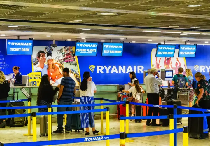 Kasa biletowa i punkty odprawy bagażu Ryanair na lotnisku, z ludźmi i bagażami.