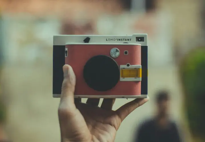Una mano tiene una Lomo'Instant. Cosa significa "fotocamera ai"? Questa fotocamera istantanea, con il suo design retrò, cattura momenti unici.