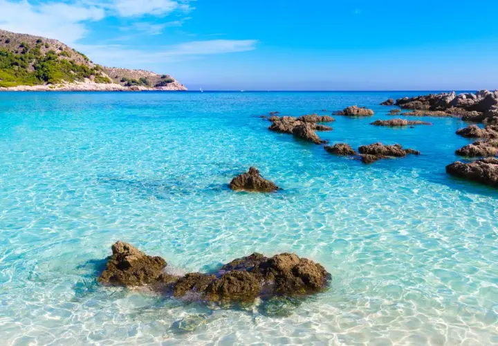 Eau turquoise cristalline, rochers émergeant de la mer, colline verdoyante en arrière-plan. Un rêve de toscane plage.