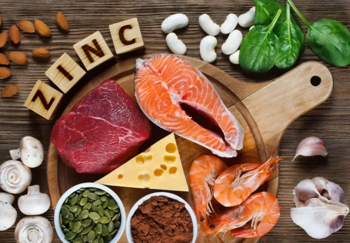 Zink-reiche Lebensmittel wie Rindfleisch, Lachs, Garnelen, Kürbiskerne, Käse, Spinat, Mandeln, Pilze und Knoblauch sind auf einem Holztisch arrangiert.