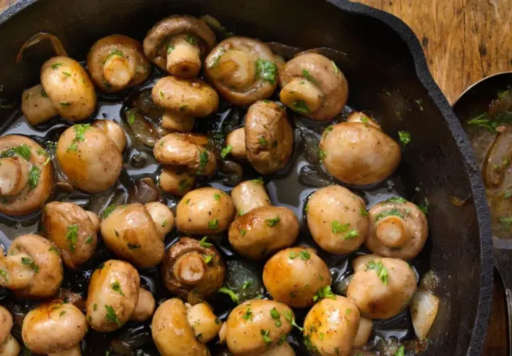 Champiñones al ajillo recién hechos en sartén de hierro fundido, con perejil picado y un toque de ajo.