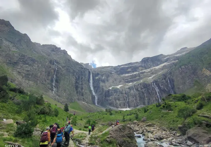 Senderos de Gavarnie: excursionistas caminan hacia impresionantes cascadas en un valle montañoso.