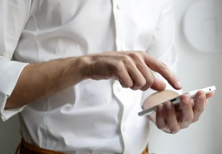 Mężczyzna w białej koszuli prowadzi rozmowę telefoniczną po angielsku, dotykając ekranu smartfona.