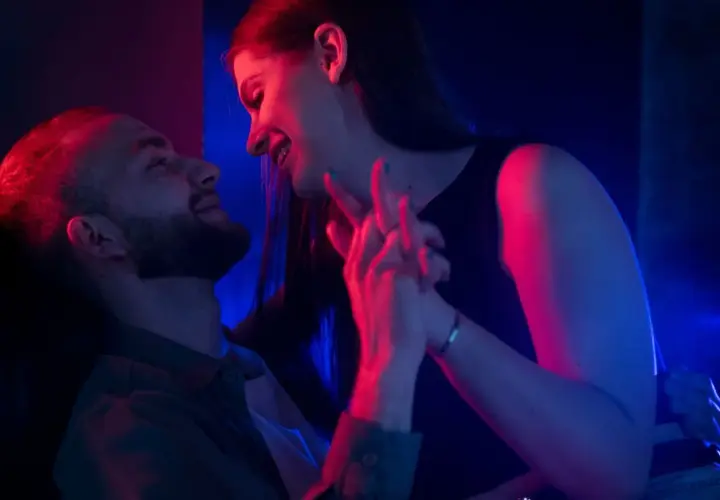Para zbliża się do siebie w blasku neonów. Ich dłonie splatają się, tworząc intymną chwilę, która sugeruje seks bez penetracji.