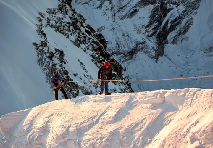 Dwóch alpinistów na śnieżnym grzbiecie, przygotowuje się do wspinaczki na Mera Peak. Słońce oświetla zbocza.