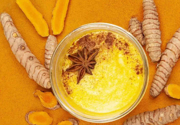 Goldene Milch mit Kurkuma und Honig, verziert mit Sternanis. Umgeben von frischen Kurkumawurzeln und Pulver.