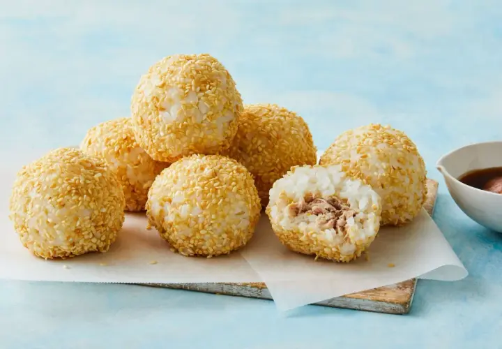 A delicious tuna bento box features rice balls coated in sesame seeds, with one cut open to reveal the tuna filling.