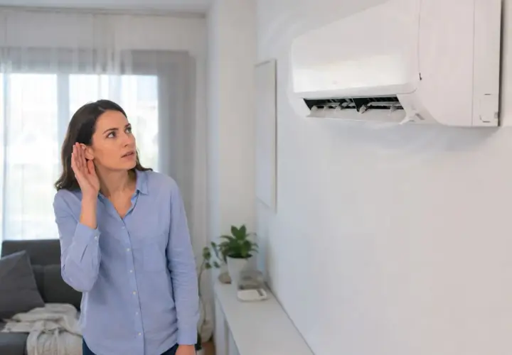 Mujer escucha atentamente el **ruido del aire acondicionado**, preocupada por un sonido inusual.