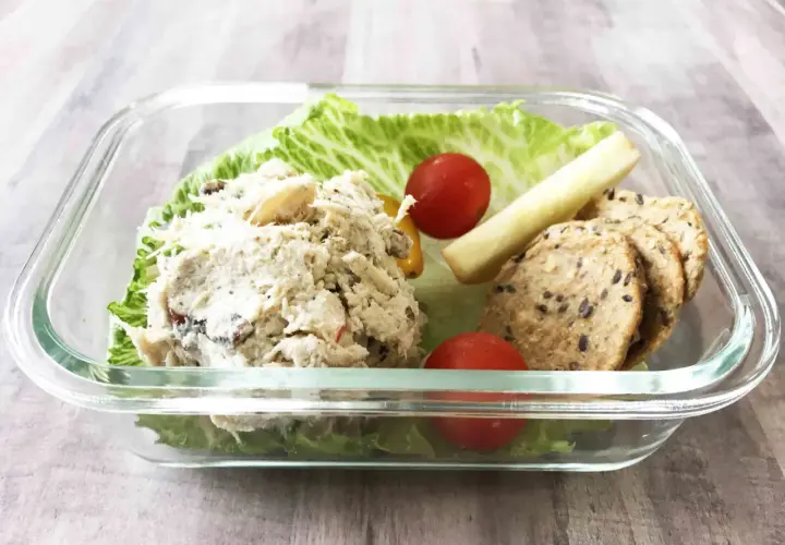 A delicious chicken salad bento box with lettuce, cherry tomatoes, a pickle spear, and crackers.