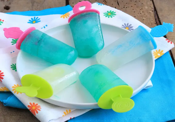 Cinque ghiaccioli senza zucchero, colorati e rinfrescanti, su un piatto bianco, pronti per un'estate sana e gustosa.