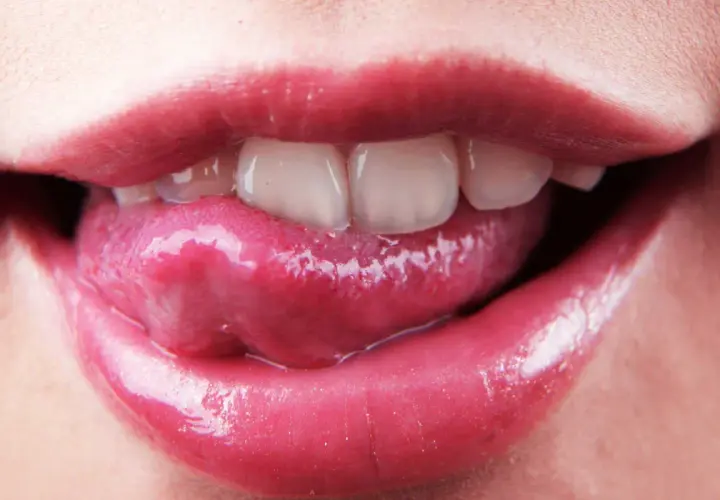 Labbra lucide e lingua che esce, mostrando i denti. La saliva è disinfettante, un piccolo segreto di bellezza naturale.