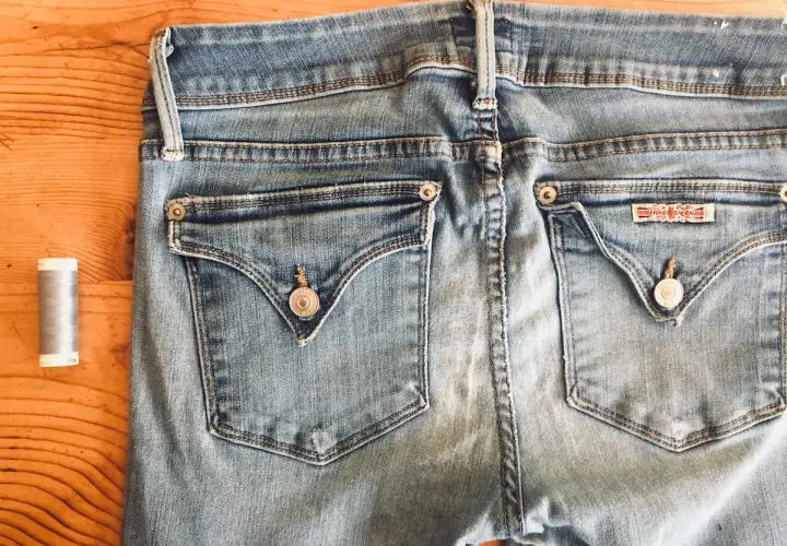 A spool of grey thread sits beside the back pockets of light blue jeans, ready for invisible mending.