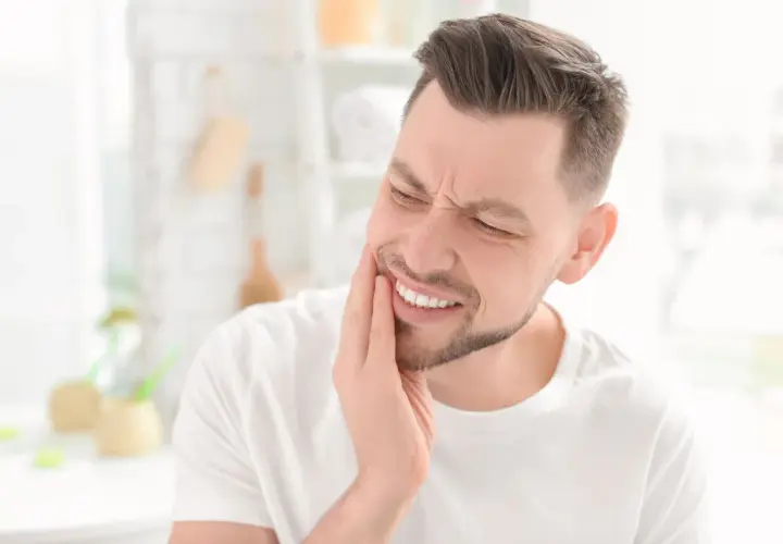 Uomo con mano sulla guancia, espressione di dolore ai denti, forse un problema al solco gengivale.