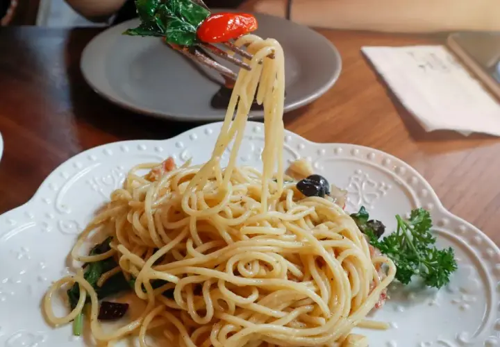 Widok z bliska na talerz pysznego spaghetti aglio e olio, z widelcem unoszącym porcję makaronu z bazylią i pomidorkiem.