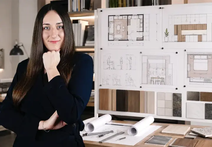 Młoda studentka architektury zamyślona nad projektami wnętrz, planszami z wizualizacjami i próbkami materiałów.