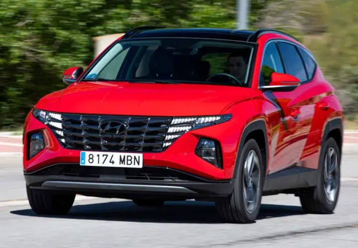 Un conductor prueba el Hyundai Tucson híbrido enchufable rojo, con su distintiva parrilla y luces LED, circulando por una carretera.