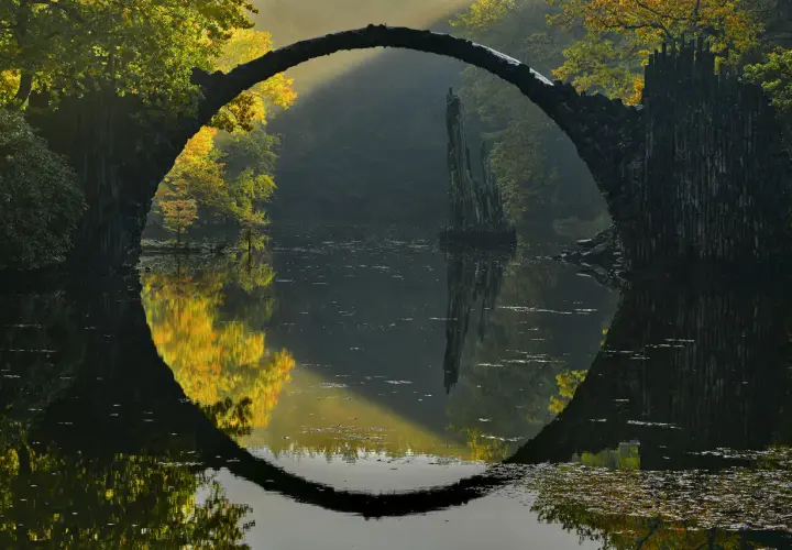 Kamienny most tworzy idealne koło z odbiciem w wodzie. Magiczny krajobraz jesienny, uchwycony przez doświadczonego **fotografa krajobrazu**.