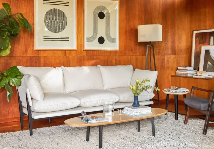 A modern living room with a white sofa, art, and a floor lamp, all set against warm wood tones.