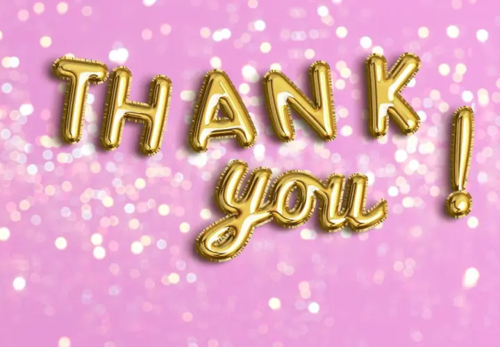 Globos dorados forman las palabras de agradecimiento "Thank you!" sobre un fondo rosa con luces bokeh.