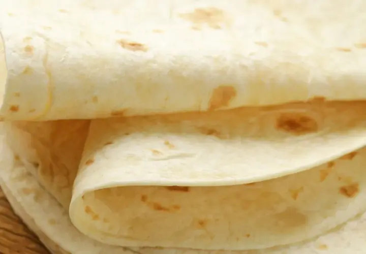Stos cienkich, jasnych placków tortilli na drewnianym blacie. Czy tortilla jest zdrowsza od chleba? Zależy od składników!