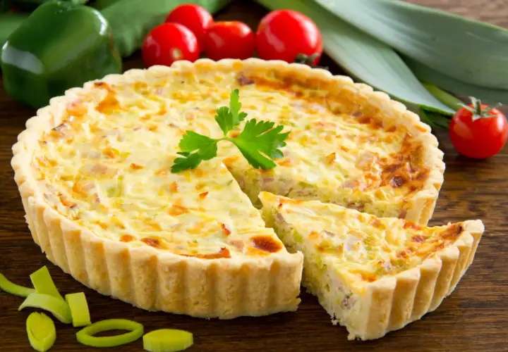 Quiche Lorraine con pasta sfoglia, un classico della cucina francese, con una fetta tagliata per mostrare il ripieno cremoso e saporito.