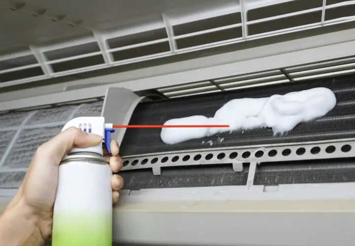Mano rociando espuma limpiadora en las aletas de un aire acondicionado para limpiar bandeja aire acondicionado.
