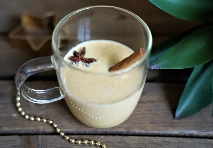 Un verre de lait de poule crémeux, garni d'anis étoilé et d'un bâton de cannelle, sur fond de bois rustique.
