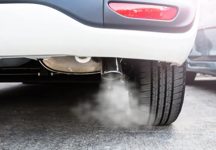 Białe auto pluje wodą z wydechu. Para wodna wydobywa się z rury wydechowej, tworząc mgiełkę wokół opony.