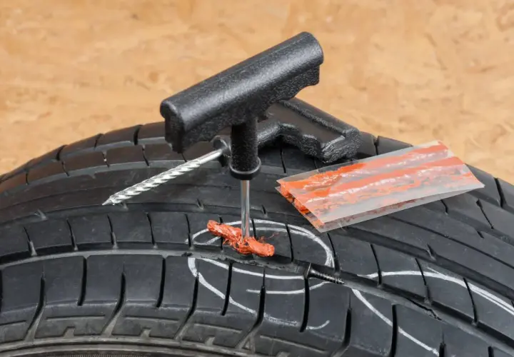Kit de réparation pour pneu de voiture : un outil insère une mèche dans un pneu crevé.