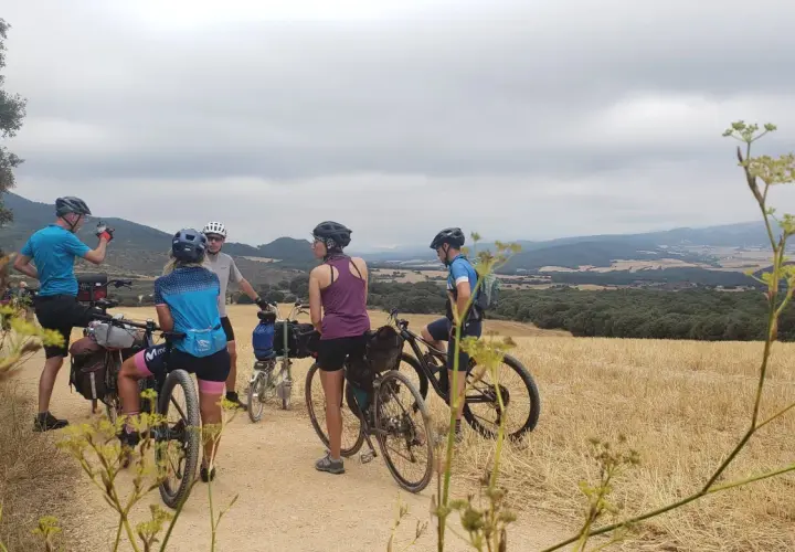 Ciclistas en ruta por la EuroVelo 6, disfrutando del paisaje rural y las colinas bajo un cielo nublado.