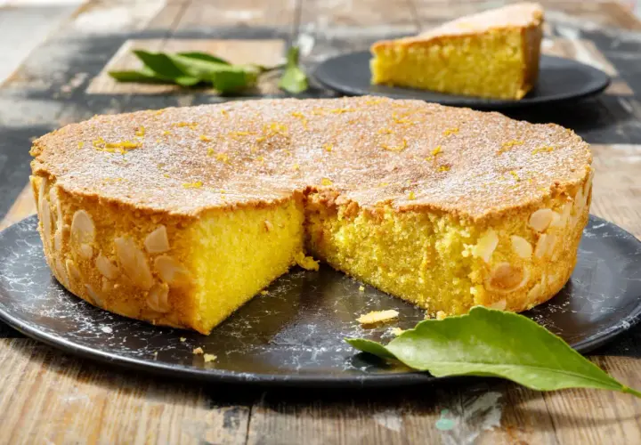 Deliziosa caprese al limone, con mandorle tostate sui bordi e scorza d'arancia in superficie, spolverata di zucchero a velo.