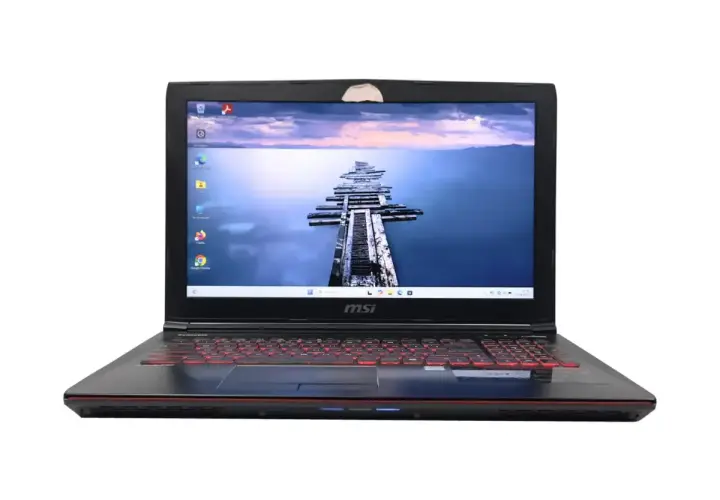 Czarny laptop MSI z podświetlaną na czerwono klawiaturą. Na ekranie widok na drewniane molo. Zastanawiasz się, jaki Windows do starego laptopa?