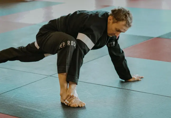 Mężczyzna w czarnym kimonie wykonuje rozciąganie. To część jego planu treningowego pod sporty walki, przygotowującego ciało do dynamicznych ruchów.