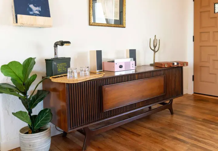 A mid-century modern wood console with a record player, speakers, and a fiddle leaf fig plant.