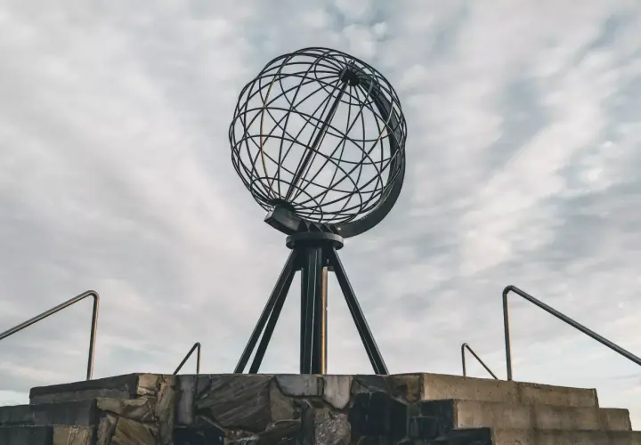 Metalowy glob na statywie na tle pochmurnego nieba, widok z dołu.