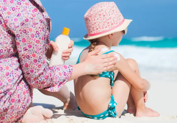Mamma applica la crema solare a una bambina sulla spiaggia, prevenendo la dermatite da sabbia.