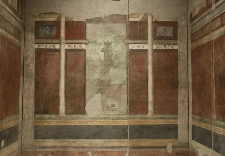 Affresco nella casa di Livia: colonne, pannelli rossi e un paesaggio centrale con un albero e un vaso.