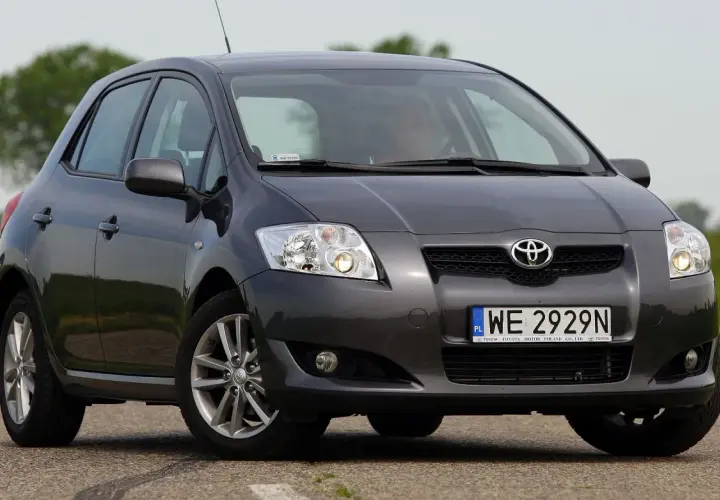 Szary Toyota Auris 2015 na drodze, z zielonym polem w tle.
