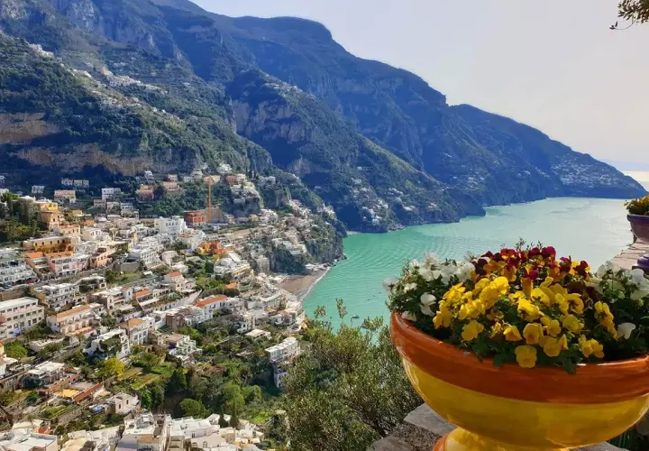 Colorful flowers bloom overlooking Positano, a stunning town cascading down the cliffs. This view offers inspiration for where to stay in Amalfi Coast.