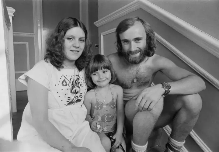 Phil Collins z żoną i córką, uśmiechnięci, siedzą na schodach.