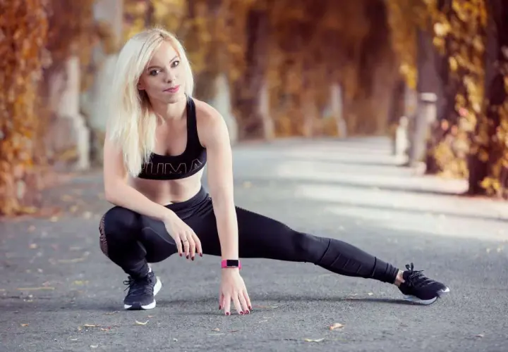 Blondynka w sportowym stroju wykonuje ćwiczenia rozciągające. Jej trening spinningowy jest gotowy do rozpoczęcia w jesiennej alei.