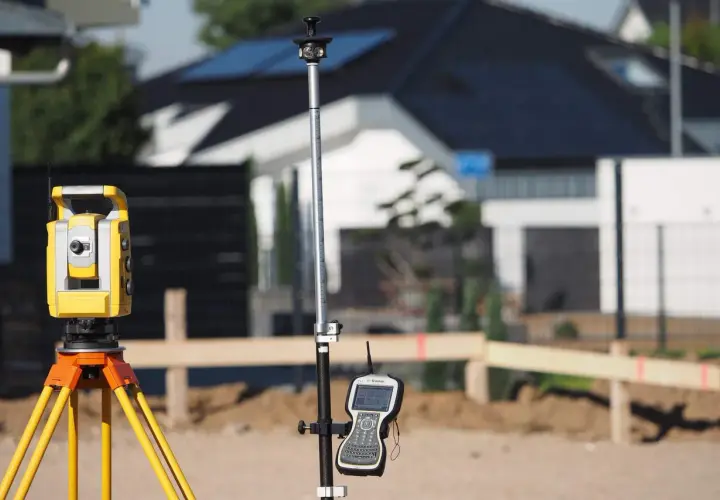 Żółty tachimetr geodezyjny i tyczka z odbiornikiem GPS na budowie.