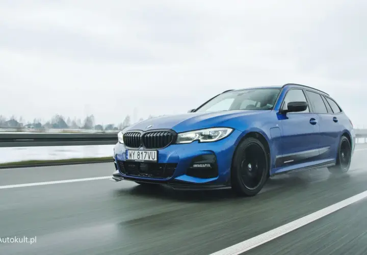 Niebieskie BMW 330e na mokrej drodze, z widocznymi kroplami deszczu na karoserii.