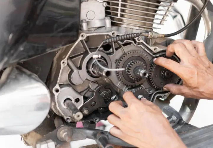 Mani che lavorano sul motore di una moto, ingranaggi visibili. Possibili cause di perdita potenza motore diesel.
