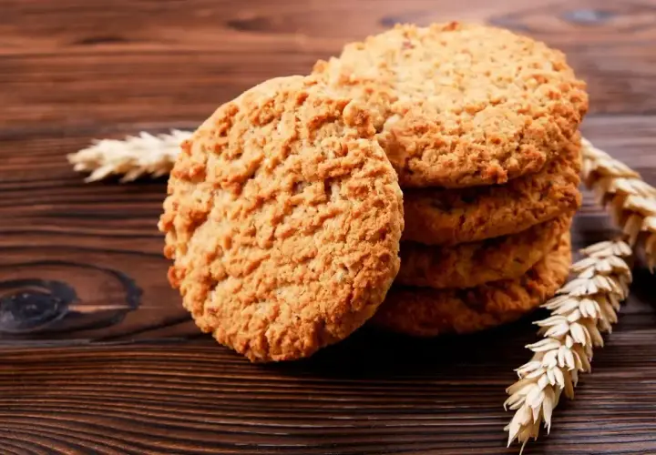 Biscotti integrali da colazione dorati e croccanti, impilati su un tavolo di legno scuro, con spighe di grano a lato.