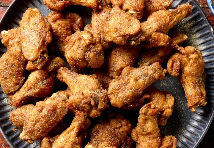A pile of crispy, golden-brown Nagoya style chicken wings, seasoned with spices, on a dark plate.