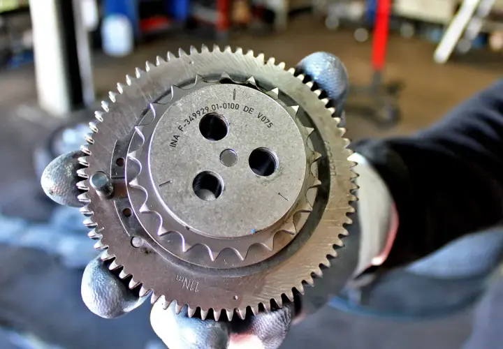 Zużyty łańcuch rozrządu objawia się wyślizganymi zębami koła. Mechanik pokazuje element z widocznymi śladami zużycia.